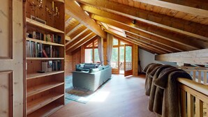 A spacious attic room with wooden beams, a large window, a sofa, and a bookshelf.
