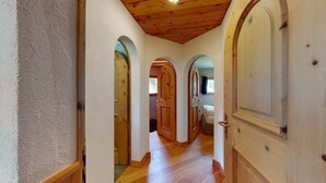 A hallway with wooden floors, white walls, and wooden doors with arched tops.