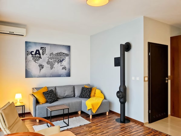 A modern living room with a grey sofa, a black standing fan, a world map artwork, and a wooden floor.