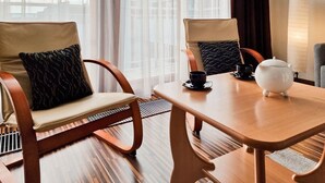 A hotel room with two wooden chairs with cushions, a wooden table with a teapot and cups, and a view of buildings through sheer curtains. - 1-room apartment WO13C - Platan (WO13C) (Swinoujscie)