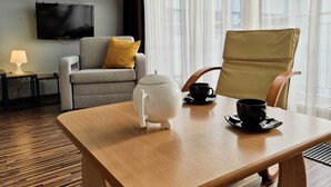 A hotel room with a wooden table, a sofa with a yellow pillow, a white teapot, two black cups, and a television on the wall. - 1-room apartment WO13C - Platan (WO13C) (Swinoujscie)