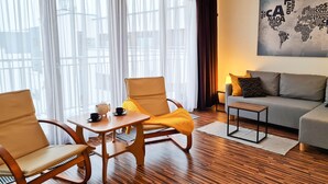 A modern living room with a wooden floor, a sofa, two rocking chairs, a small table with a teapot and cups, and a world map artwork on the wall. - 1-room apartment WO13C - Platan (WO13C) (Swinoujscie)