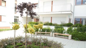 A courtyard with a bench, various shrubs, and a tree. - 1-room apartment WO13C - Platan (WO13C) (Swinoujscie)