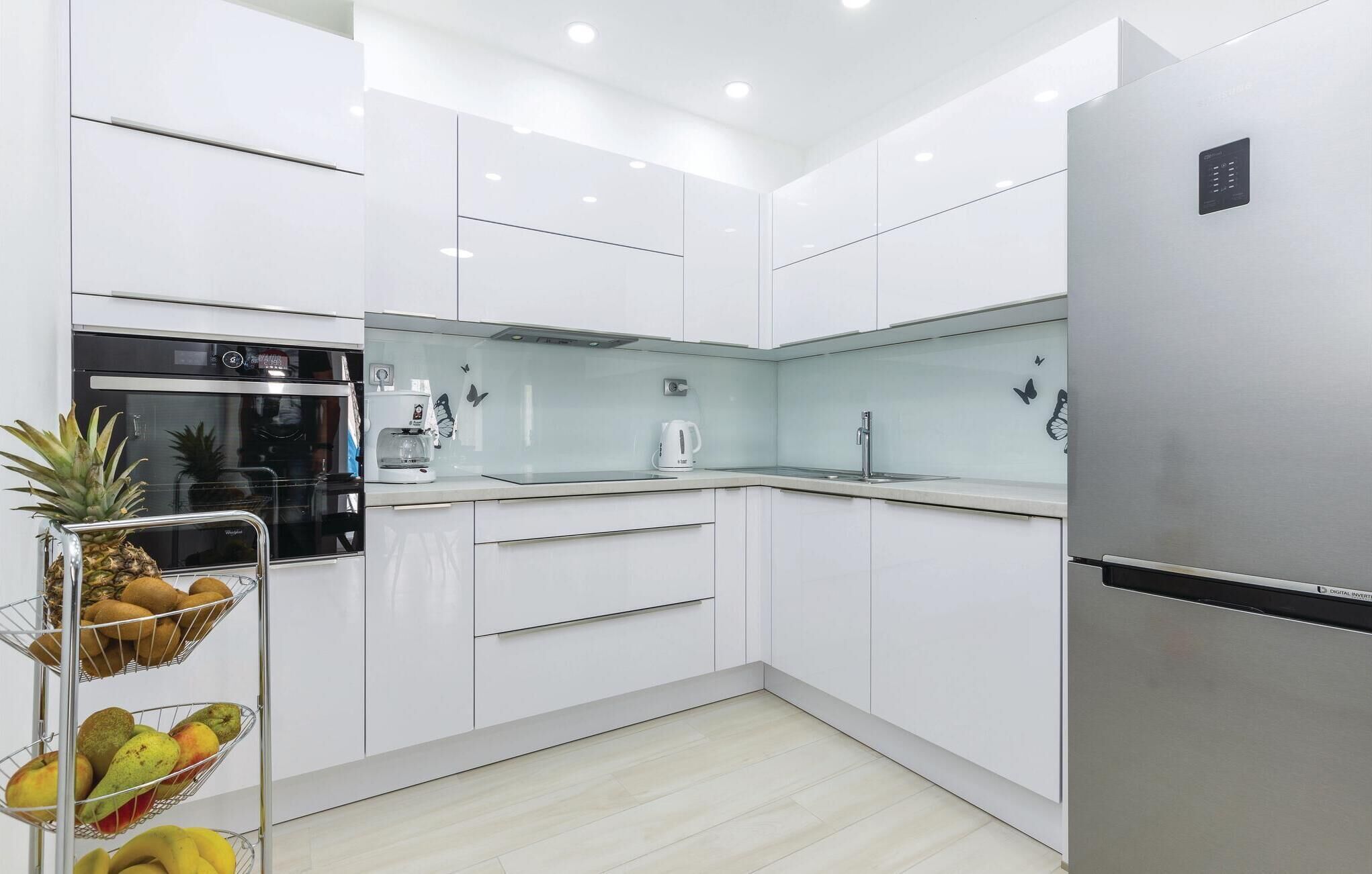 Uma cozinha moderna com armários brancos, geladeira de aço inoxidável, forno embutido e cafeteira.