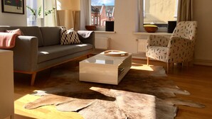 Ein Wohnzimmer mit einer Couch, einem Couchtisch, einem gemusterten Sessel, einem Fellteppich und einem gerahmten Bild von Helsinki.