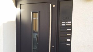 Eine schwarze Tür mit vertikalem Griff und kleinem Fenster.