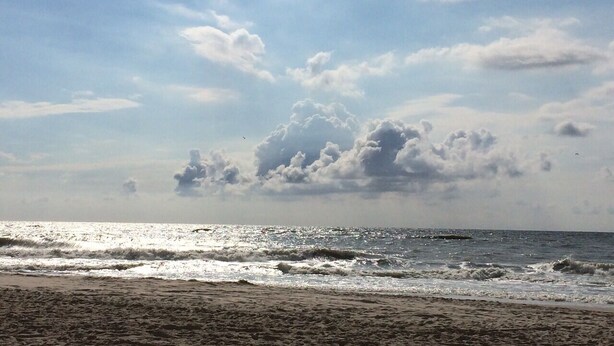 Ein Strand mit Wellen und einem teilweise bewölkten Himmel.