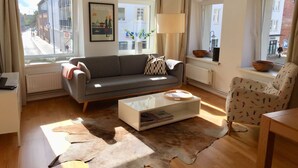 Ein Wohnzimmer mit grauem Sofa, einem weißen Couchtisch, einem gemusterten Sessel, einem Fellteppich und einem gerahmten Bild an der Wand.