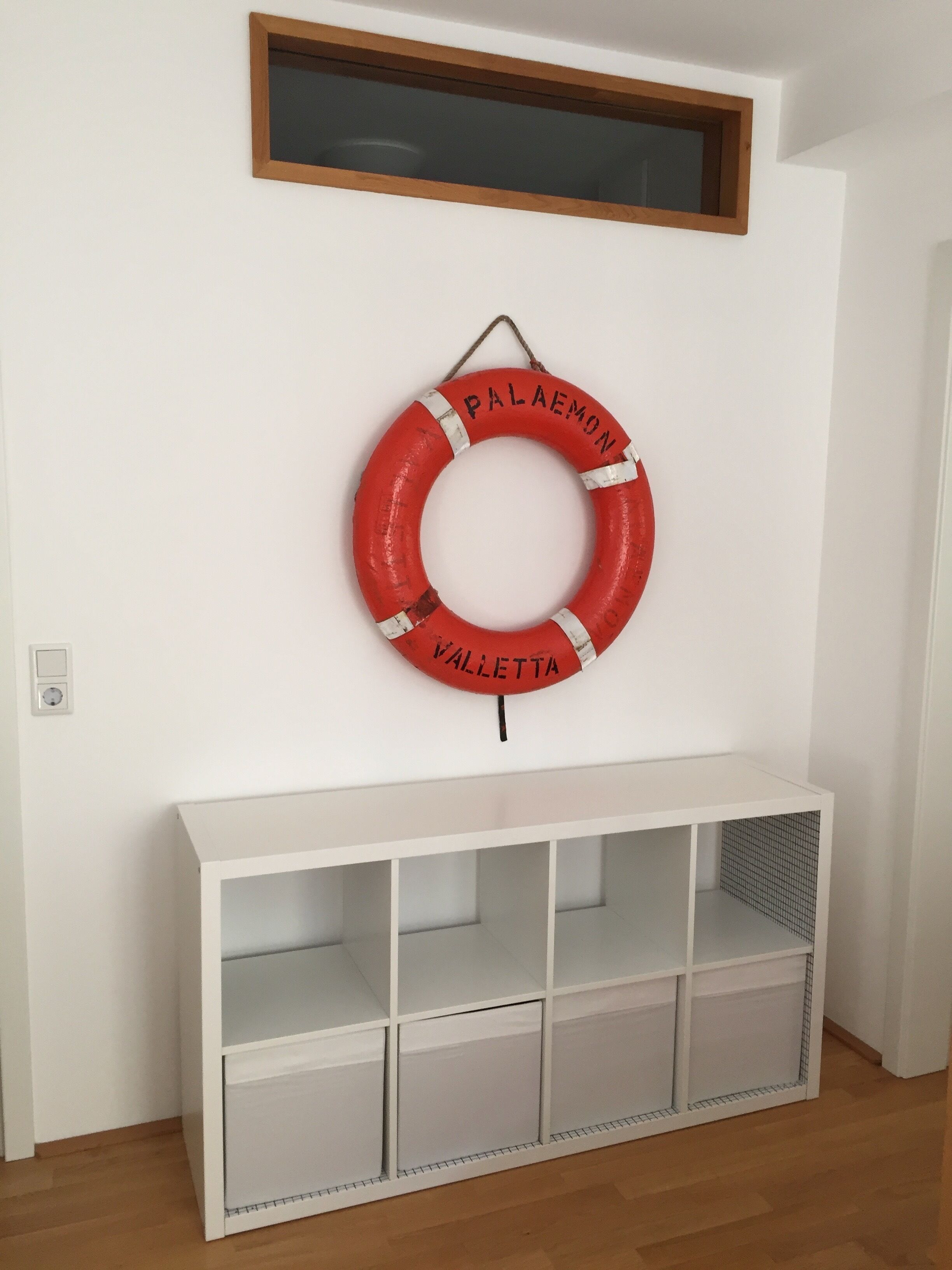 A white console table with multiple shelves and a red life ring with "PALAEMON" and "VALLETTA" text.