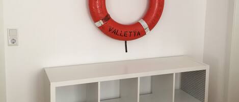 A white console table with multiple shelves and a red life ring with "PALAEMON" and "VALLETTA" text.