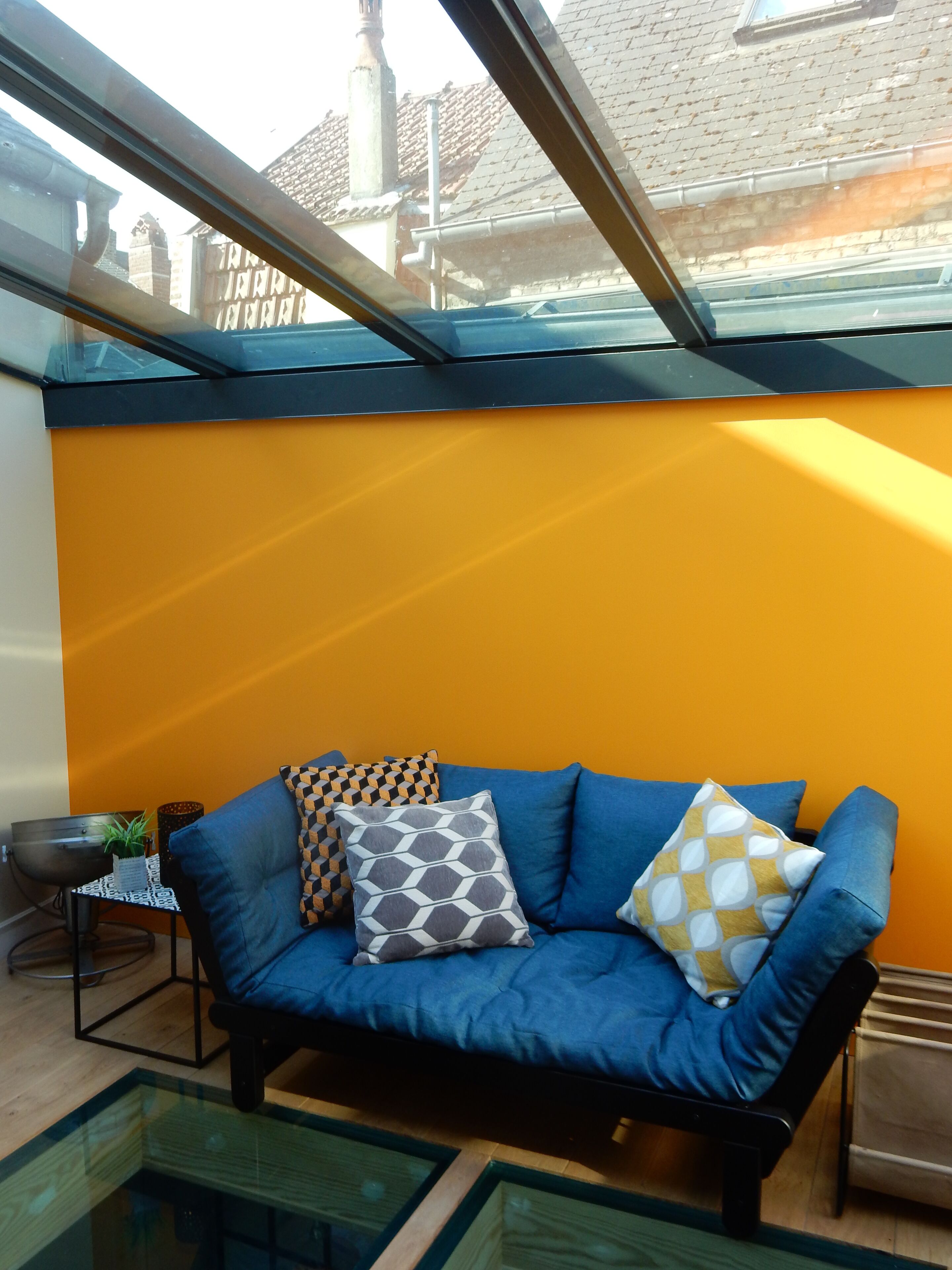 Una sala moderna con un sofá azul, cojines estampados y una mesa de vidrio.
