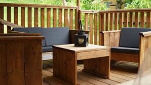 A wooden deck with a sofa and a table, a lantern, and a view of greenery. - Cottage 5p comfort in beautiful area with pool (le buisson de cadouin)