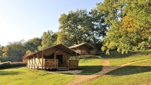 Two wooden cabins with balconies, set on a grassy hill with trees in the background. - Cottage 5p comfort in beautiful area with pool (le buisson de cadouin)