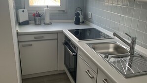 Cuina petita amb armaris blancs, forn encastrat, fogó i vàter d'acer inoxidable.