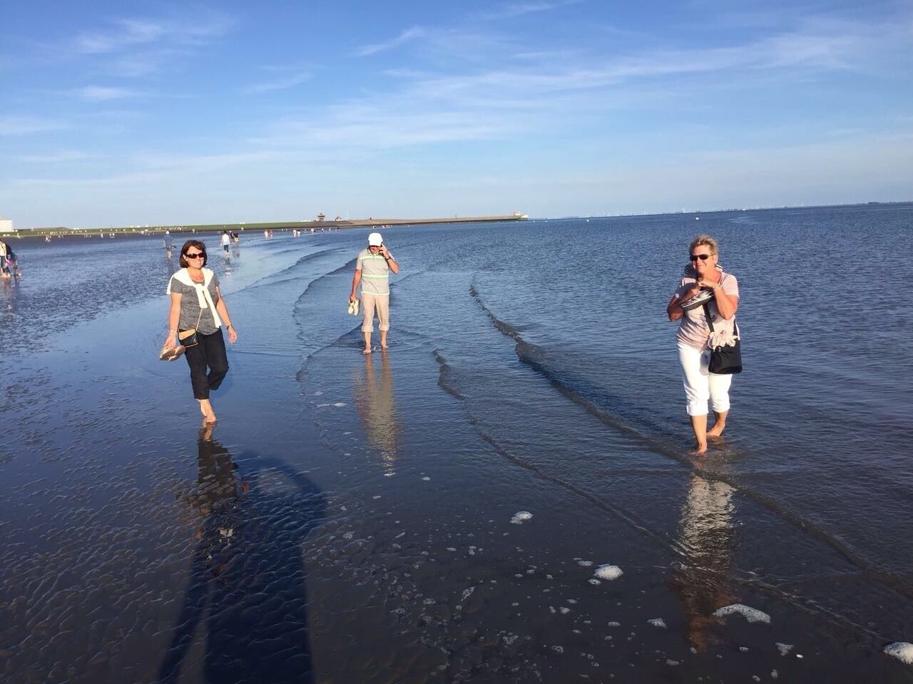 En strand där folk promenerar i det grunda vattnet.