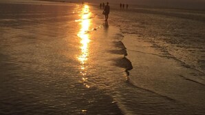 Una platja al capvespre amb gent caminant vora la riba.