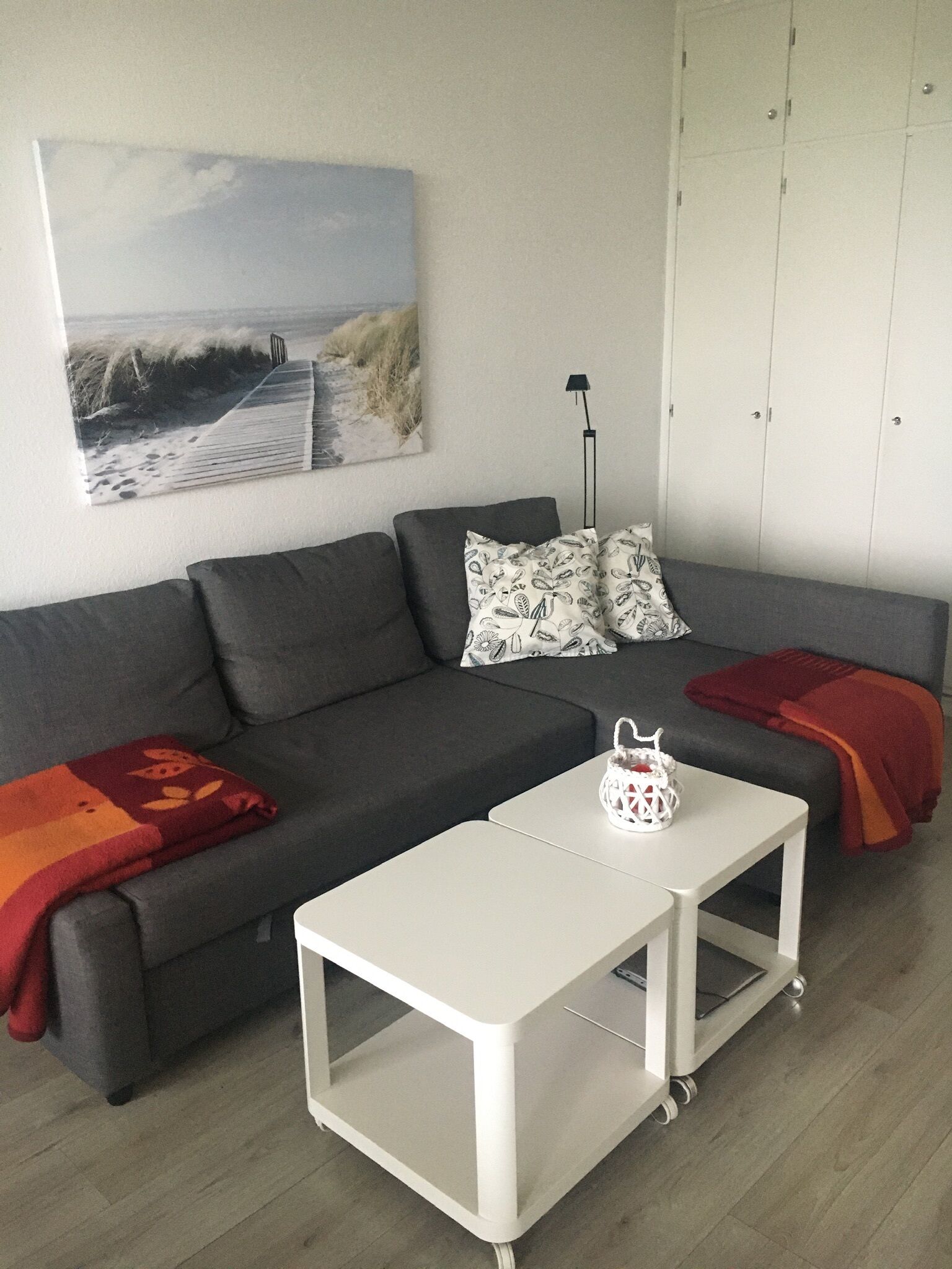 Un salon moderne avec un canapé gris, une table basse blanche et un tableau sur le thème de la plage accroché au mur.