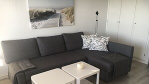 Un saló modern amb un sofà gris fosc, dues taules laterals blanques i una obra d'art mural amb temàtica de platja.