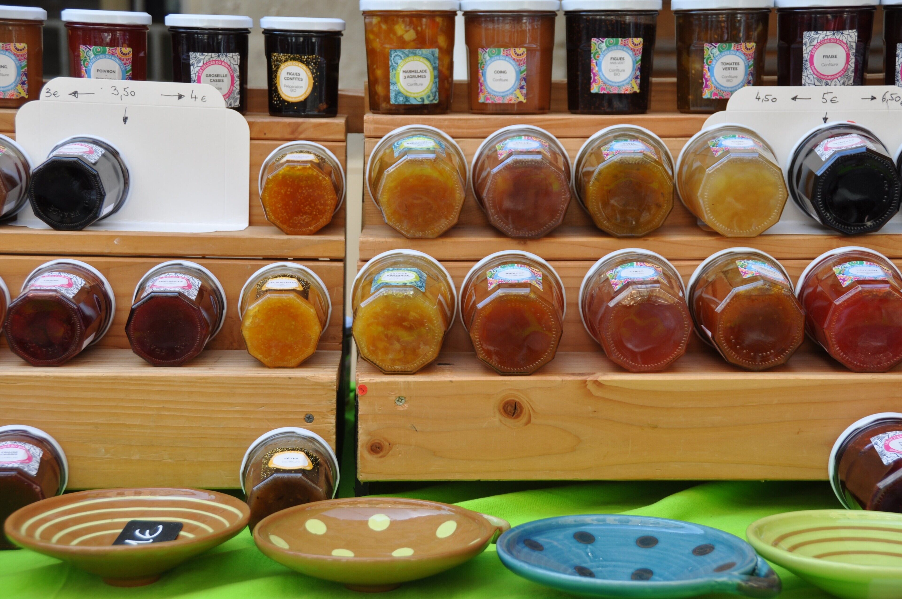 A display of various jars of preserves on wooden shelves with price tags.
