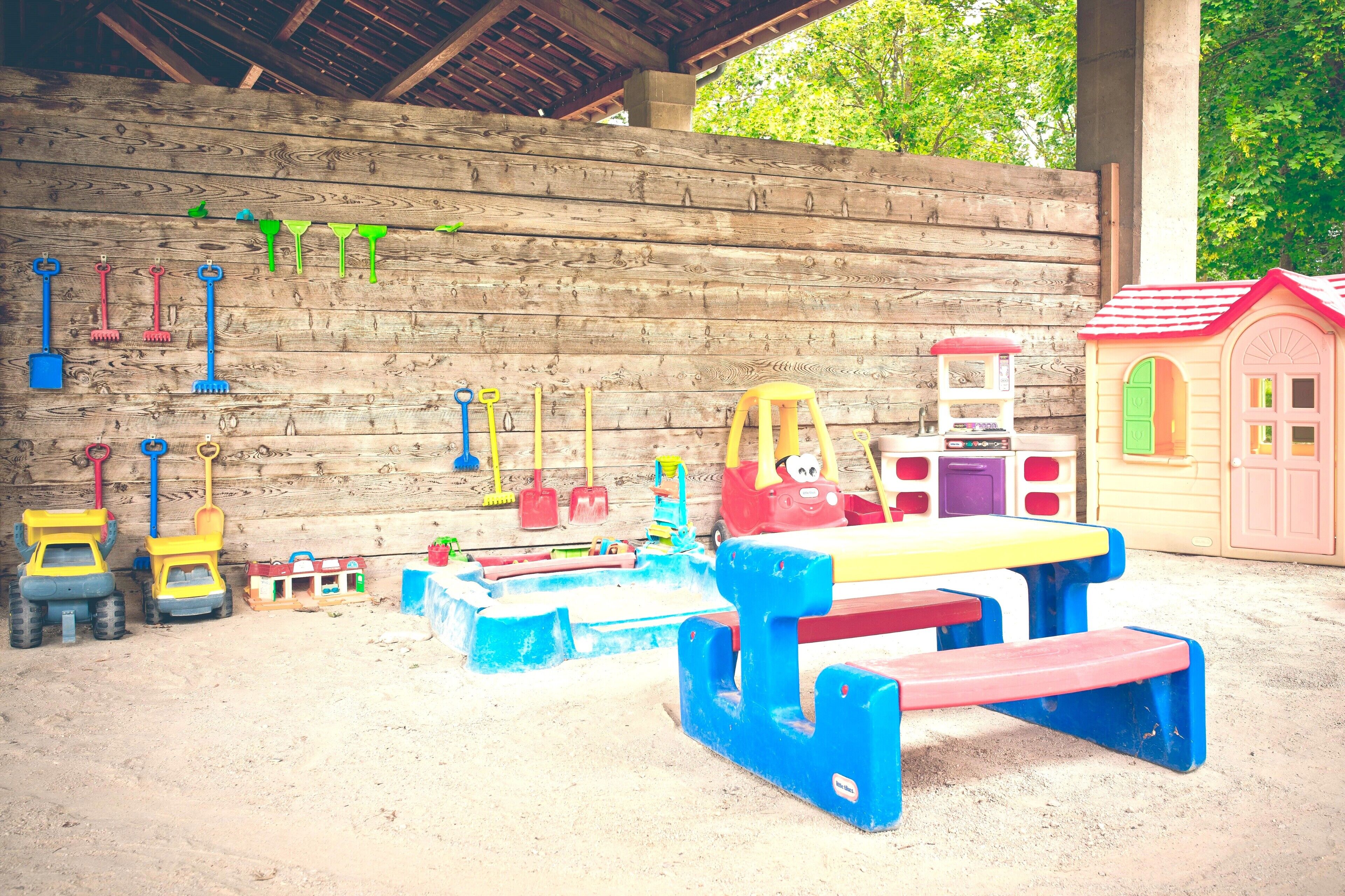 Zona de juegos infantiles con arena, juguetes y un muro de madera.
