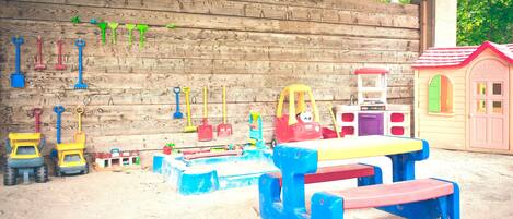 Zona de juegos infantiles con arena, juguetes y un muro de madera.