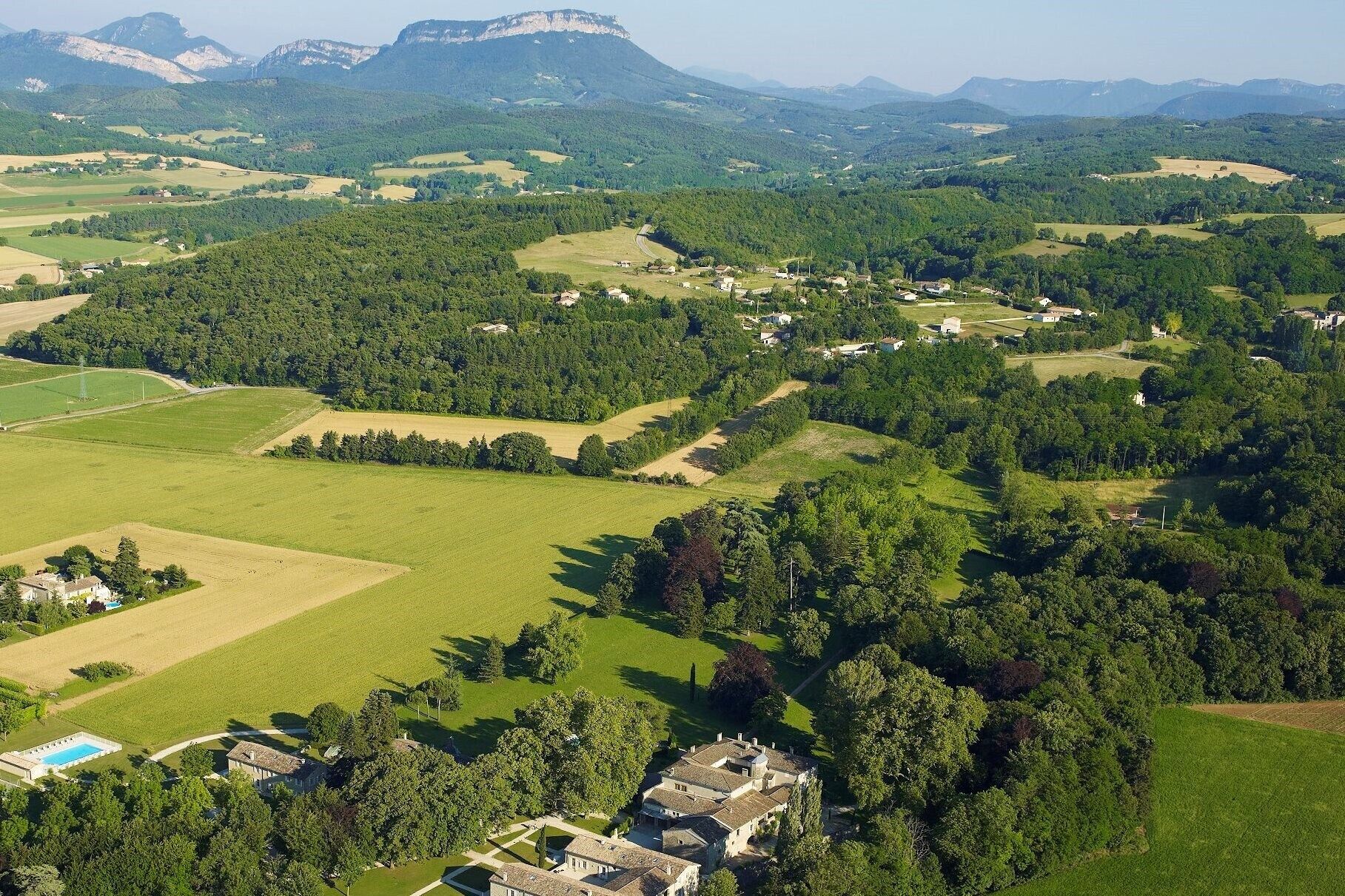 An aerial view of a rural area with scattered houses, fields, and a large estate with a swimming pool.