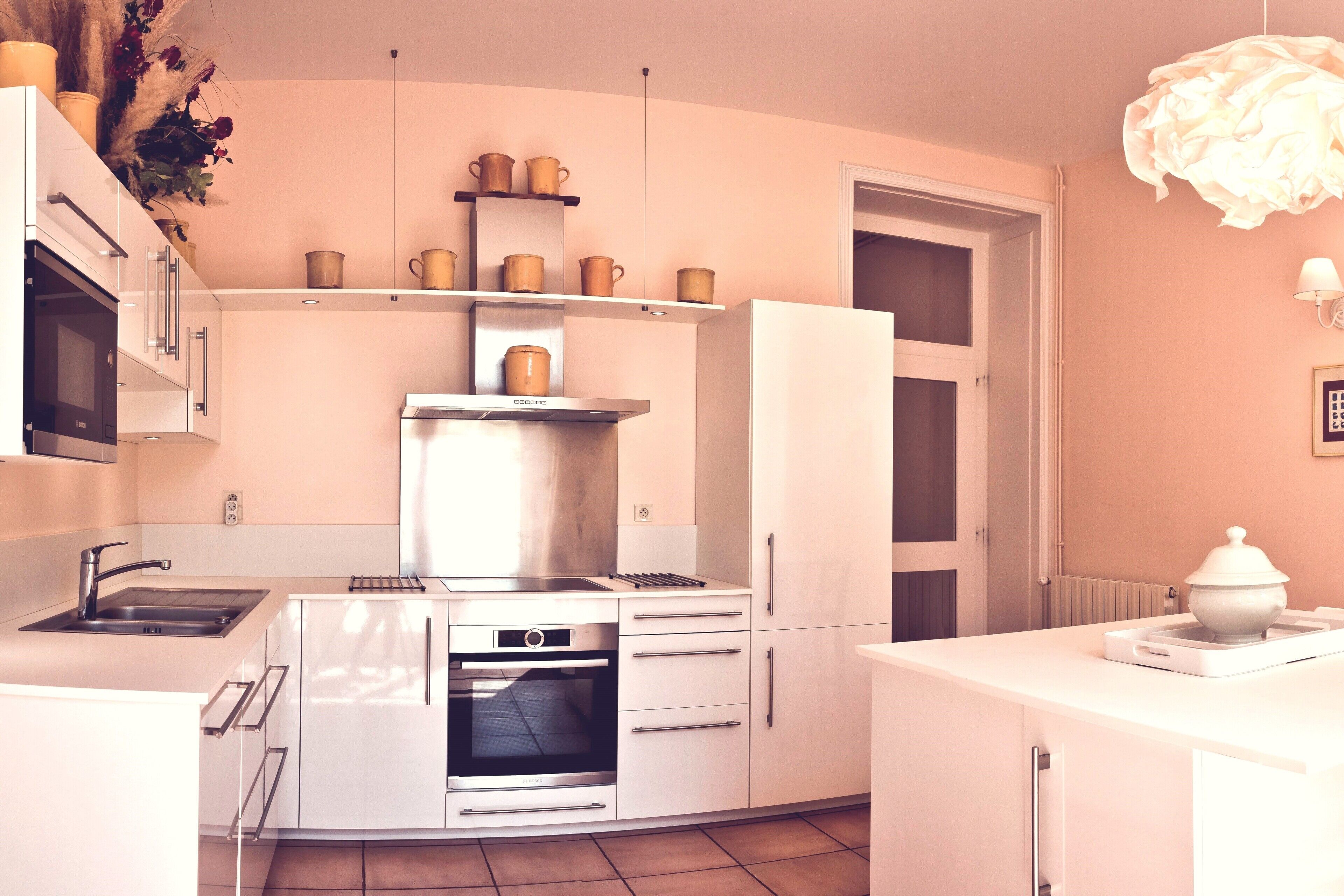 A modern kitchen with white cabinets, a stainless steel range hood, and a built-in oven. There are shelves above the sink holding pots and pans.