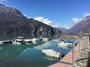 A marina with boats docked, a stone pier, and mountains in the background.
