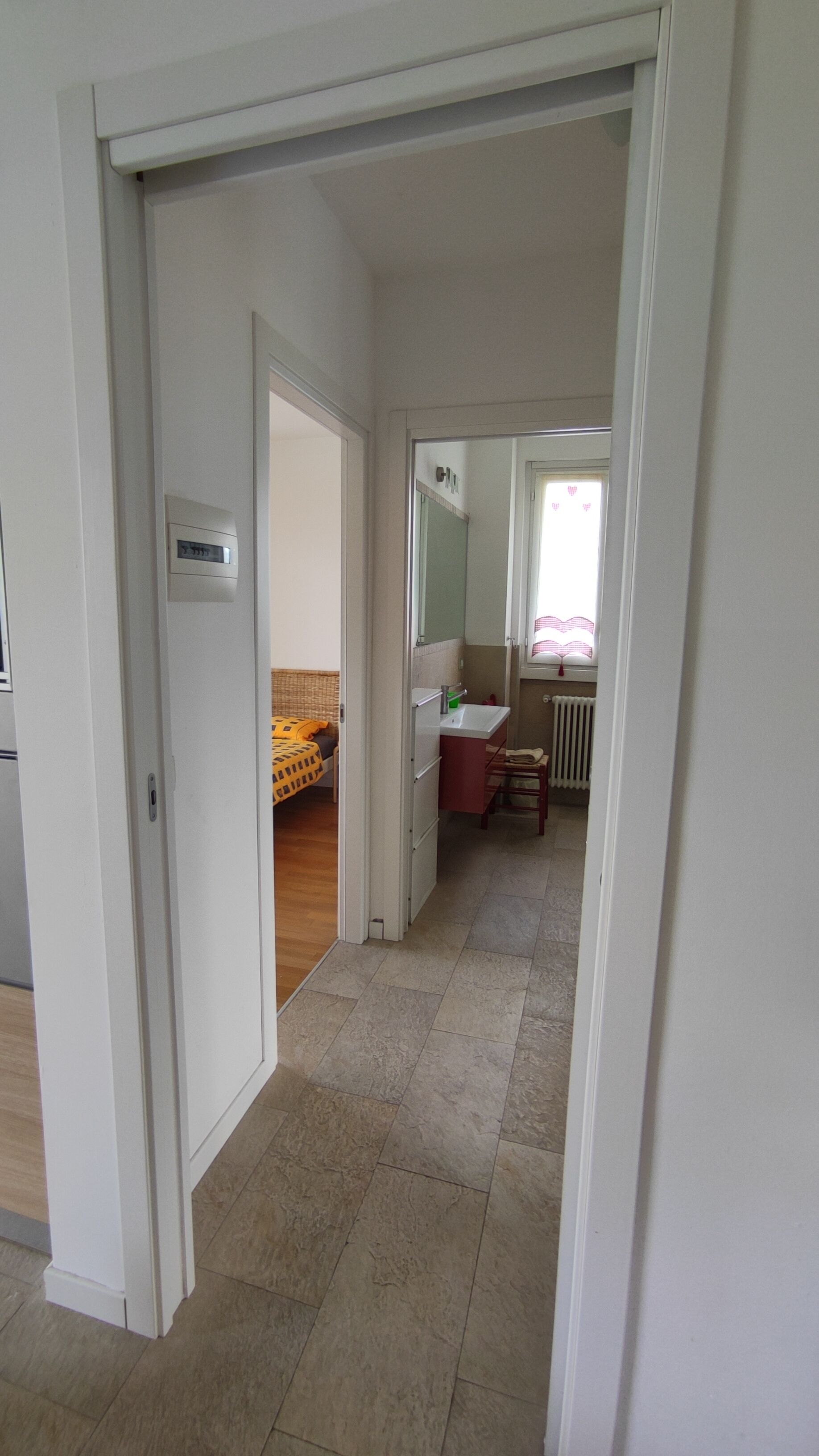 A hallway leading to a bedroom with a bed, a bathroom with a sink, and a radiator.