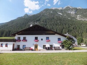 Un bâtiment blanc avec un toit en pente, de nombreuses fenêtres et des jardinières sur la façade.