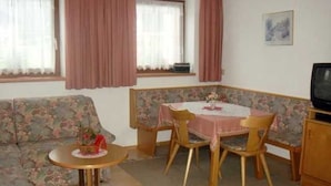 Une pièce comprenant un canapé à motifs floraux, une petite table ronde, une table à manger avec des chaises, un téléviseur et une fenêtre avec des rideaux.