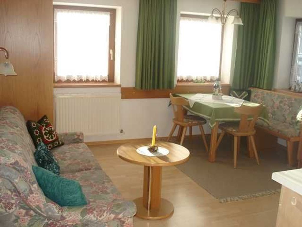A living room with a sofa, a round table, a dining table with chairs, and a window with curtains.