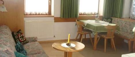 Una sala de estar con un sofá, una mesa redonda, una mesa de comedor con sillas y una ventana con cortinas.