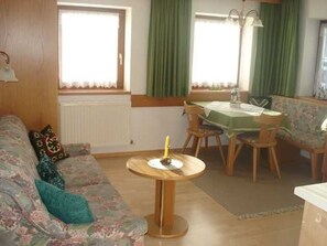 Una sala de estar con un sofá, una mesa redonda, una mesa de comedor con sillas y una ventana con cortinas.