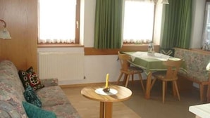 Un salon comprenant un canapé, une table ronde, une table à manger avec des chaises et une fenêtre avec des rideaux.
