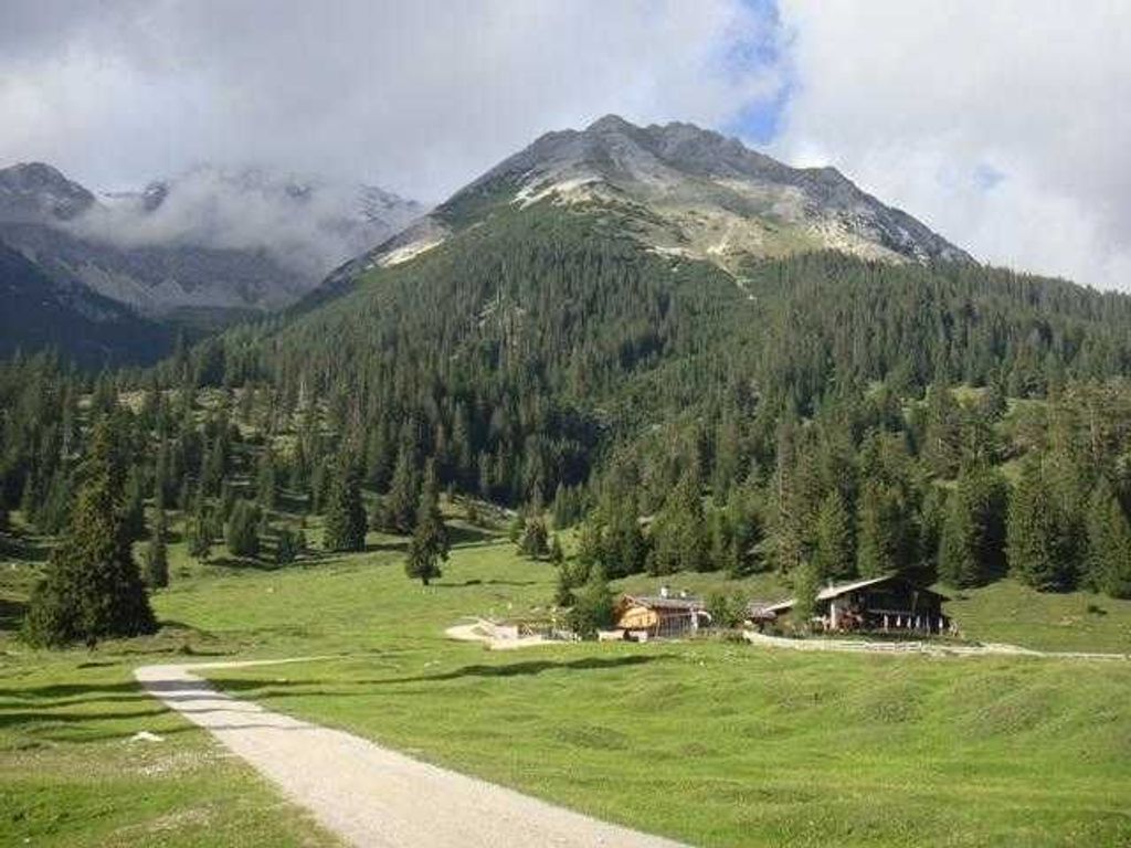 A mountain landscape with a dirt path leading to a rustic building surrounded by trees.