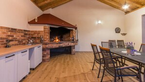 Uma cozinha com forno de tijolos, teto de madeira e um espaço de refeições com cadeiras e mesa.