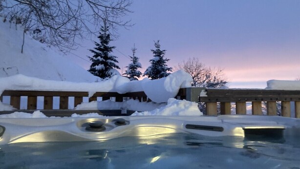 Un jacuzzi cubierto parcialmente por nieve, con una terraza de madera al fondo.