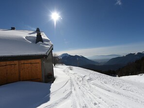 Une cabane en bois dont le toit est recouvert de neige, avec un ciel dégagé et une vue sur les montagnes.