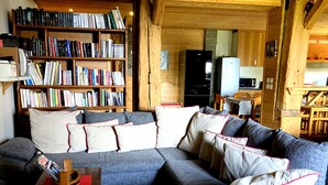 Un soggiorno accogliente con un divano componibile, una libreria in legno piena di libri e un angolo cottura sullo sfondo.