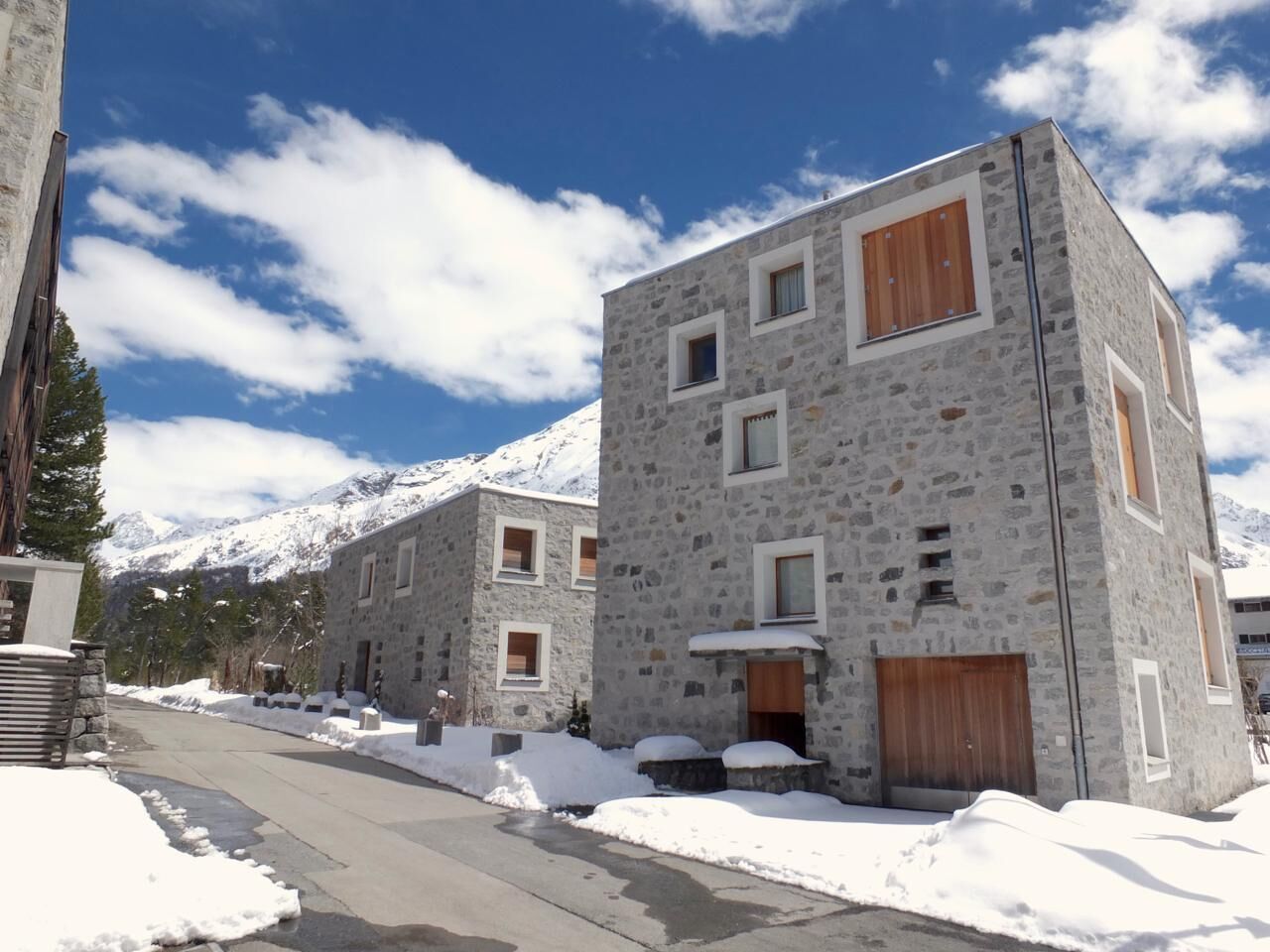 A snow-covered street with stone buildings, a clear sky, and mountains in the background.
