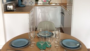 Un coin repas avec une table ronde dressée pour quatre personnes, agrémentée d’assiettes, de couverts et de verres.