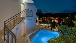 A modern building with a swimming pool, a staircase, and a view of a waterfront at night. - Villa with private swim pool, 40 meters from the sea (Seget Vranjica)
