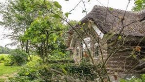 Un edificio rústico de piedra con techo de paja, rodeado de abundante vegetación y árboles.