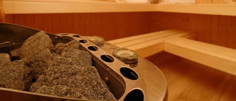 A sauna room with wooden walls, benches, and a stone heating element.