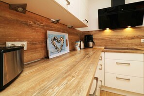A modern kitchen with wooden cabinets, a stainless steel coffee maker, and a flat-screen TV mounted above the counter.