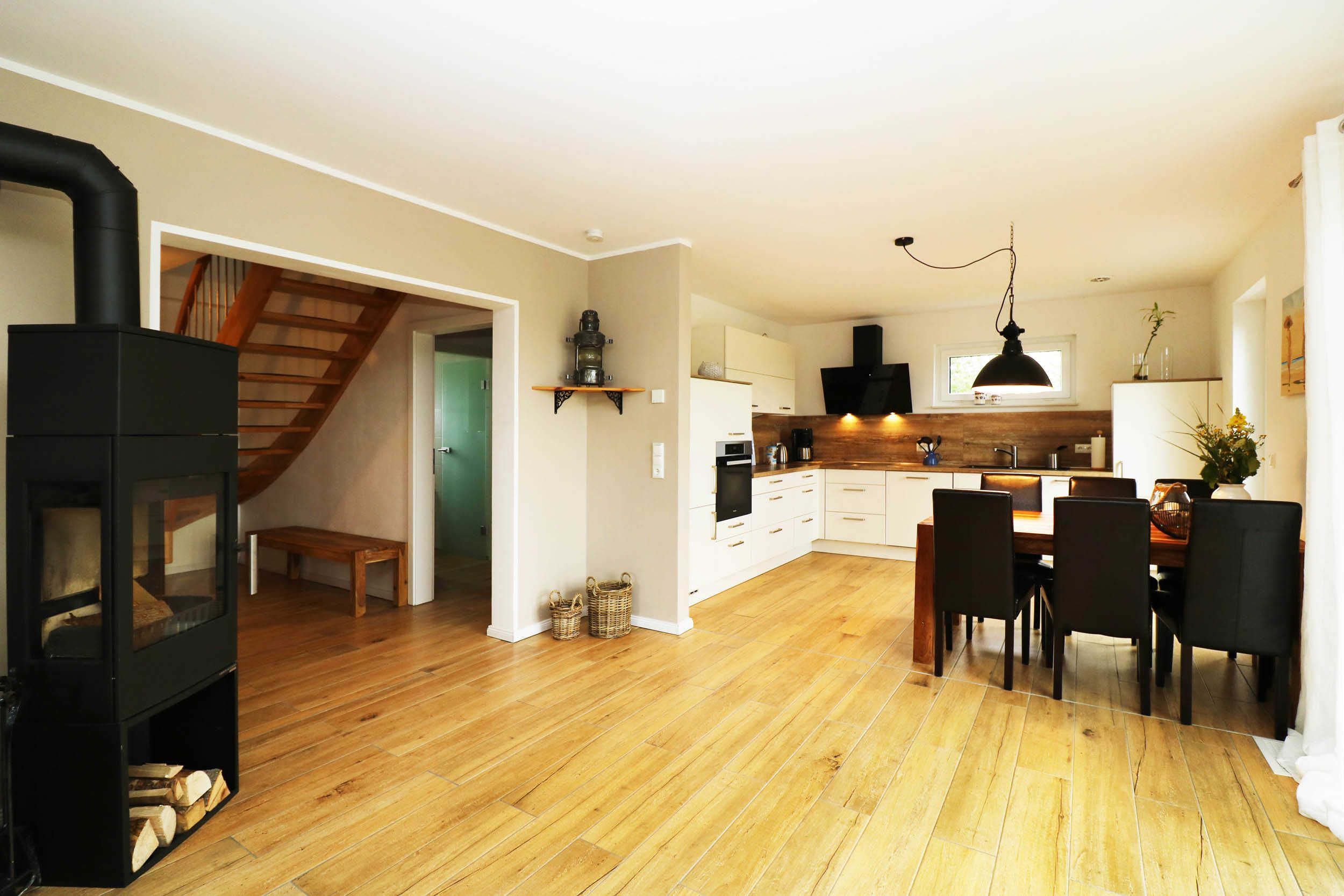 Una cocina moderna con suelo de madera, un comedor con mesa y sillas, y un estufa de leña negra.