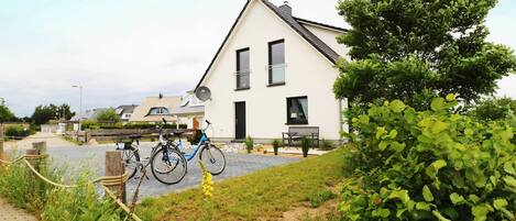 A residential area with a white house, a paved driveway, and bicycles parked in front.