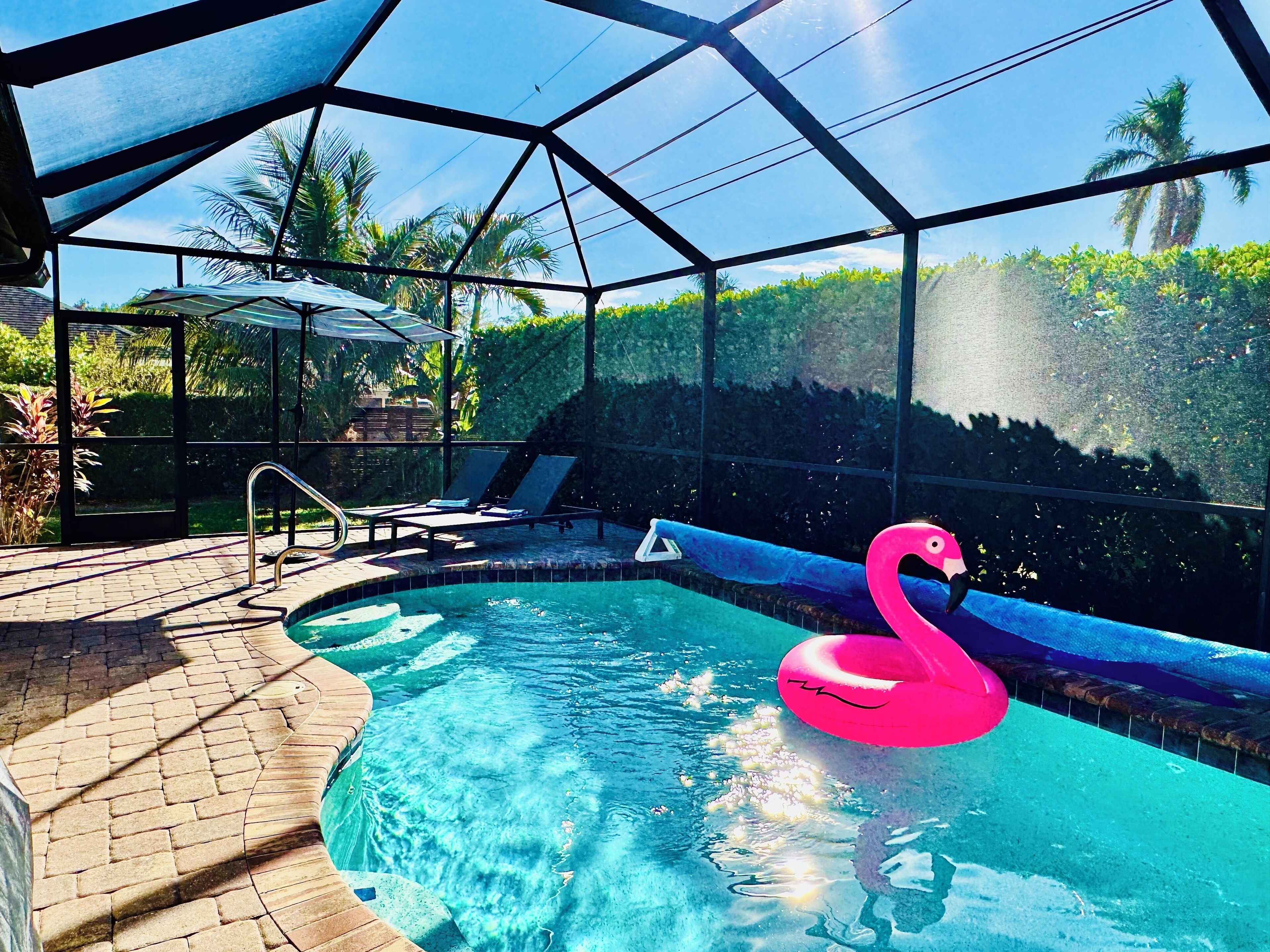 Una piscina con un flotador con forma de flamenco rosa, rodeada por una zona cubierta con sillas de descanso y un camino de ladrillo.