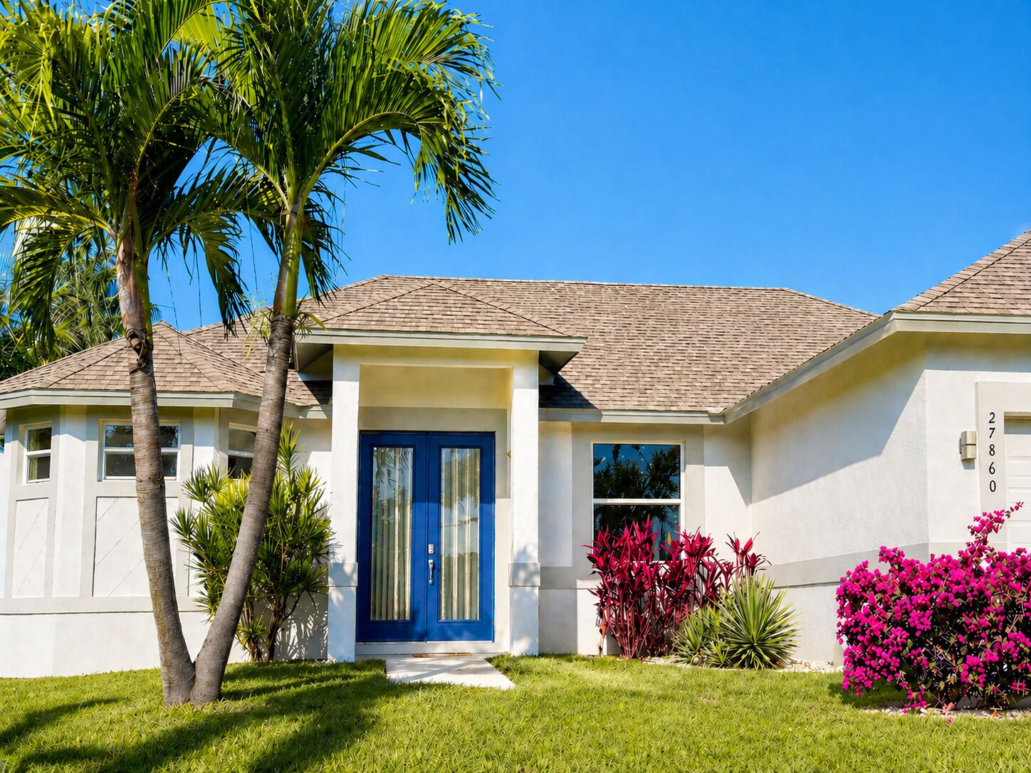 A single-story house with a blue front door, a small porch, and a well-maintained lawn.
